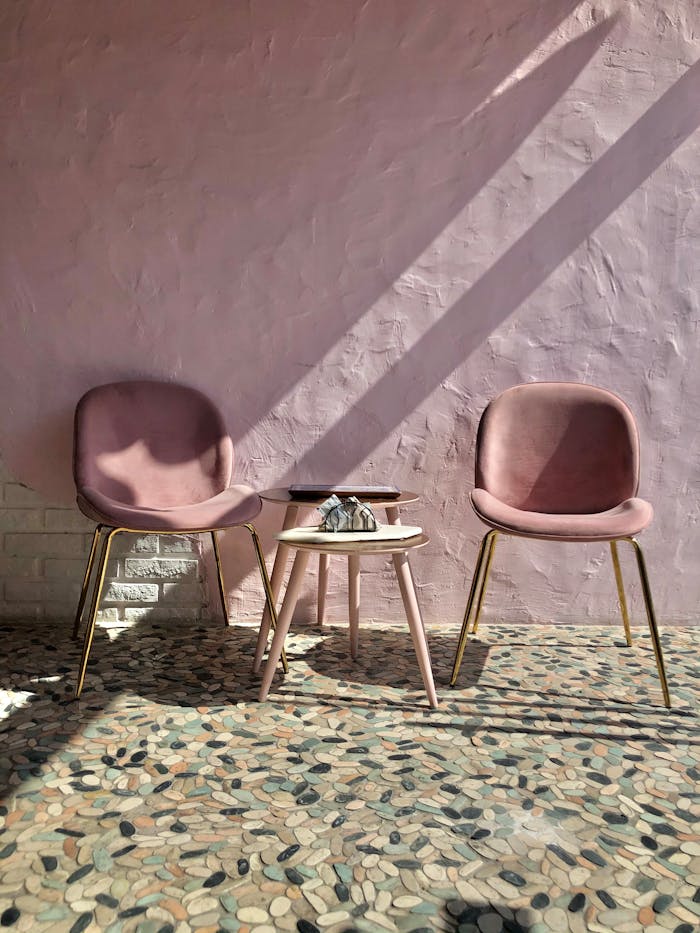 Two pink chairs and a table on patterned floor in serene lighting.